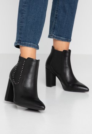 Bottines noires en cuir, dotées d'un bout pointu, d'un talon épais et de panneaux latéraux élastiques ornés de clous en argent le long des coutures.