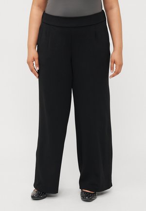 Black wide-leg trousers with a flat waistband and pleats; smooth texture with no visible patterns; paired with black studded slip-on shoes.