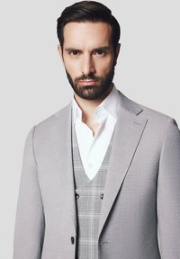 Jasnoszara marynarka w garniturze z klapkami, połączona z szarym kamizelką w kratę i białą koszulą. Gładki materiał o delikatnej fakturze i kontrastowych guzikach.