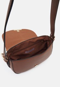 Bolso bandolera de cuero marrón con superficie texturizada, herrajes en tono dorado, cierre magnético y un interior forrado de tela marrón con un bolsillo con cremallera.