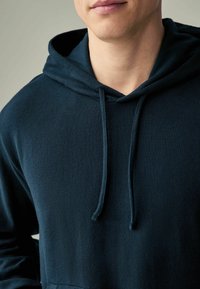 Sudadera con capucha de color azul marino con textura canalé, cordones ajustables y un corte relajado, que cuenta con un bolsillo frontal.