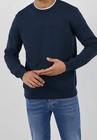 Sudadera azul marino con cuello redondo y puños acanalados. Presenta el logo en relieve "LIU JO JEANS" en la parte frontal. Tejido suave.