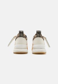 Sneaker bianchi e con stampa leopardata, dotati di suola chunky, accenti neri e un'etichetta sul tallone. Materiali testurizzati in tutta la calzature.