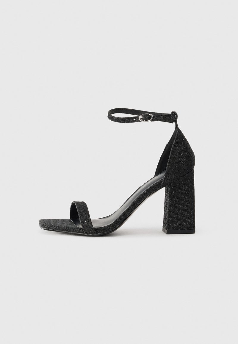 Sandal de tacón alto negro con textura brillante, que cuenta con una tira para los dedos, una tira en el tobillo y un tacón cuadrado.