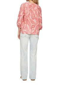 Rote und weiße Bluse mit Paisley-Muster, drei Viertel Ärmel, lockere Passform, kombiniert mit hellblauen, ausgestellten Jeans und beigen Schuhen.