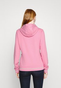 Rosa hoodie med mjuk textur, som har en dragsko i huvan, långa ärmar och en silverrand detalj vid fållen.