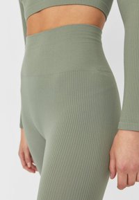 Leggings de tiro alto con textura acanalada en un suave color verde oliva, que presentan una superficie lisa y un diseño sin costuras en la cintura y las piernas.