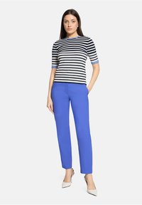 Haut en maille rayée crème et marine avec des accents bleus, associé à un pantalon bleu vif ajusté et des escarpins beige à bouts pointus.