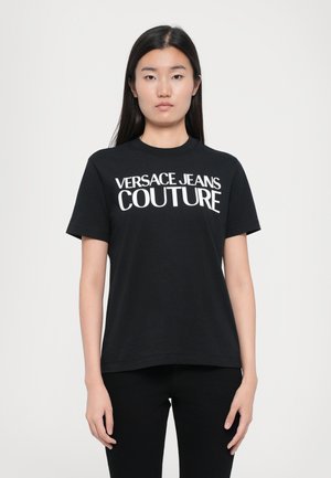 Camiseta de algodón negra con mangas cortas, cuello redondo, que presenta un texto blanco en negrita "VERSACE JEANS COUTURE" en la parte frontal.