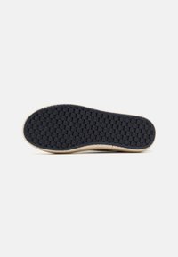 Bottom view of a shoe with a black textured rubber sole and light tan edge. Features a grid pattern for traction and durability.