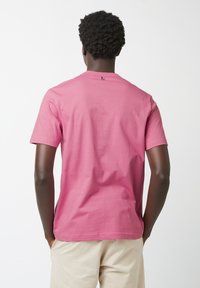 Kurzarm-T-Shirt in einfarbigem Pink, mit Rundhalsausschnitt und dezentem Rückenschild, aus weichem Baumwollstoff gefertigt.