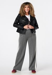 Veste de motard en cuir noir avec des zips argentés, associée à un pantalon de survêtement large gris avec des rayures blanches sur le côté et des baskets bordeaux.