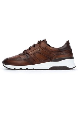 Zapatilla de cuero marrón con textura perforada, suela de goma blanca y un sutil logotipo en el lateral. Presenta un diseño con cordones y un collar acolchado.