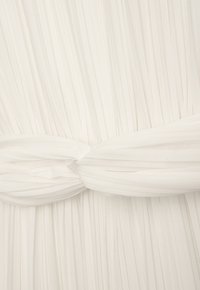 Weißer, plissierter Stoff mit einem gebundenen Bund. Die Textur wirkt weich und glatt, mit gleichmäßigen vertikalen Falten, die ein fließendes Erscheinungsbild erzeugen.