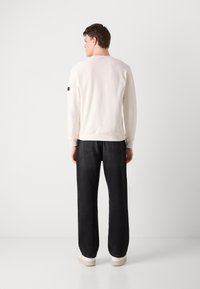 Crèmekleurige sweatshirt met een eenvoudig ontwerp, voorzien van geribbelde manchetten en zoom, gecombineerd met zwarte wijde spijkerbroek en witte sneakers.