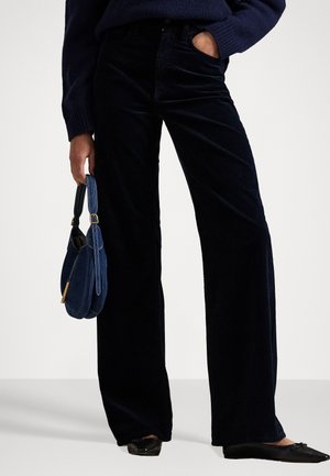 Pantaloni a gamba larga in corduroy blu scuro con sottili righe verticali, abbinati a ballerine nere e a una piccola borsa blu. Tessuto liscio e testurizzato.