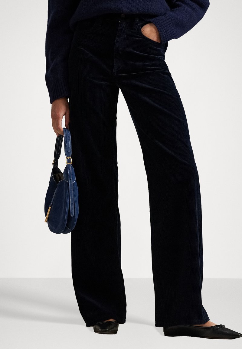 Dark navy corduroy wide-leg pants with subtle vertical lines, paired with black flats and a small blue handbag. Smooth and textured fabric.