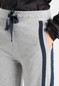 Grå sweatpants i mjukt tyg, med marinblå sidostripes, elastisk midja med dragsnöre och sidofickor.