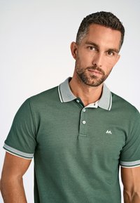 Polo verde hecho de una tela texturizada, con cuello tipo polo y ribete en blanco y gris, botonera de dos botones y un pequeño logo en el pecho.