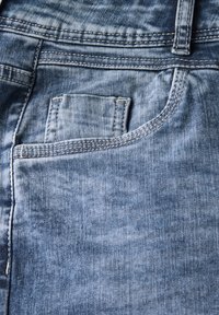 Gros plan sur une paire de jeans en denim bleu clair, mettant en avant une poche avant et des détails de couture visibles sur le tissu.