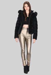 Czarna kurtka puchowa z sztucznego futra z kapturem, srebrnym zamkiem błyskawicznym i pionowym pikowaniem; zestawiona z obcisłymi spodniami w metalicznym złotym kolorze.