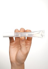 Un tubo di plastica trasparente contenente un trattamento per le labbra, tenuto in mano, con un tappo a vite bianco. Testo sul tubo: “THE GLOSSY LIP TREAT, Rivestimento idratante per labbra.”