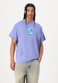 Camiseta de algodón lavanda con un estampado gráfico que incluye la palabra "sensei" y un fondo de cuadrícula azul. Corte holgado con mangas cortas.