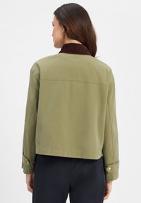 Khaki katoenjack met een bruine suède kraag, met een losse pasvorm, knoopmanchetten en een gladde, matte textuur.
