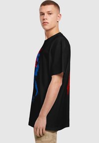 Sort t-shirt med korte ærmer, prydet med livlige blå og røde grafiske designs. Løs pasform og blødt stof med en glat tekstur.