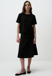 Zwarte textuur top met korte mouwen en een zwarte middellange rok. Heeft een eenvoudig ontwerp, losse pasvorm en zwarte platte schoenen.