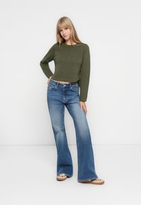 Maglione cropped verde oliva abbinato a jeans a zampa d'elefante blue chiaro. Il maglione ha una finitura testurizzata; i jeans presentano una vita alta e tasche frontali.