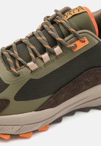 Scarpa da hiking verde e marrone con materiali in rete e suede, punta rinforzata, accenti arancioni e lacci a fantasia. Design della suola robusto.