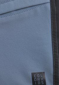 Ljust blått tyg med en slät textur, med svarta sömnadsdetaljer och en liten logotagg som står "COLOR KIDS."