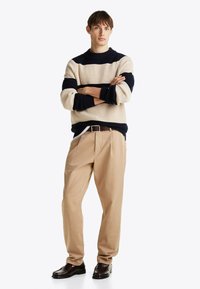 Strickpullover in Creme und Marineblau gestreift, beigere, plissierte Hose und dunkelbraune Lederloafer. Einfaches Design mit gerippter Textur und rundem Hals.