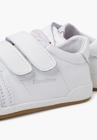Sneaker bianche in pelle con strap in velcro, punta rotonda e suole in gomma beige. Logo "Blanditos" cucito di lato. Texture liscia, design minimal.