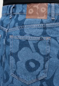 Jeansy dżinsowe z tylną kieszenią i ciemnoniebieskim kwiatowym nadrukiem, z brązową skórzaną naszywką z wytłoczonym wzorem kwiatu na pasie.