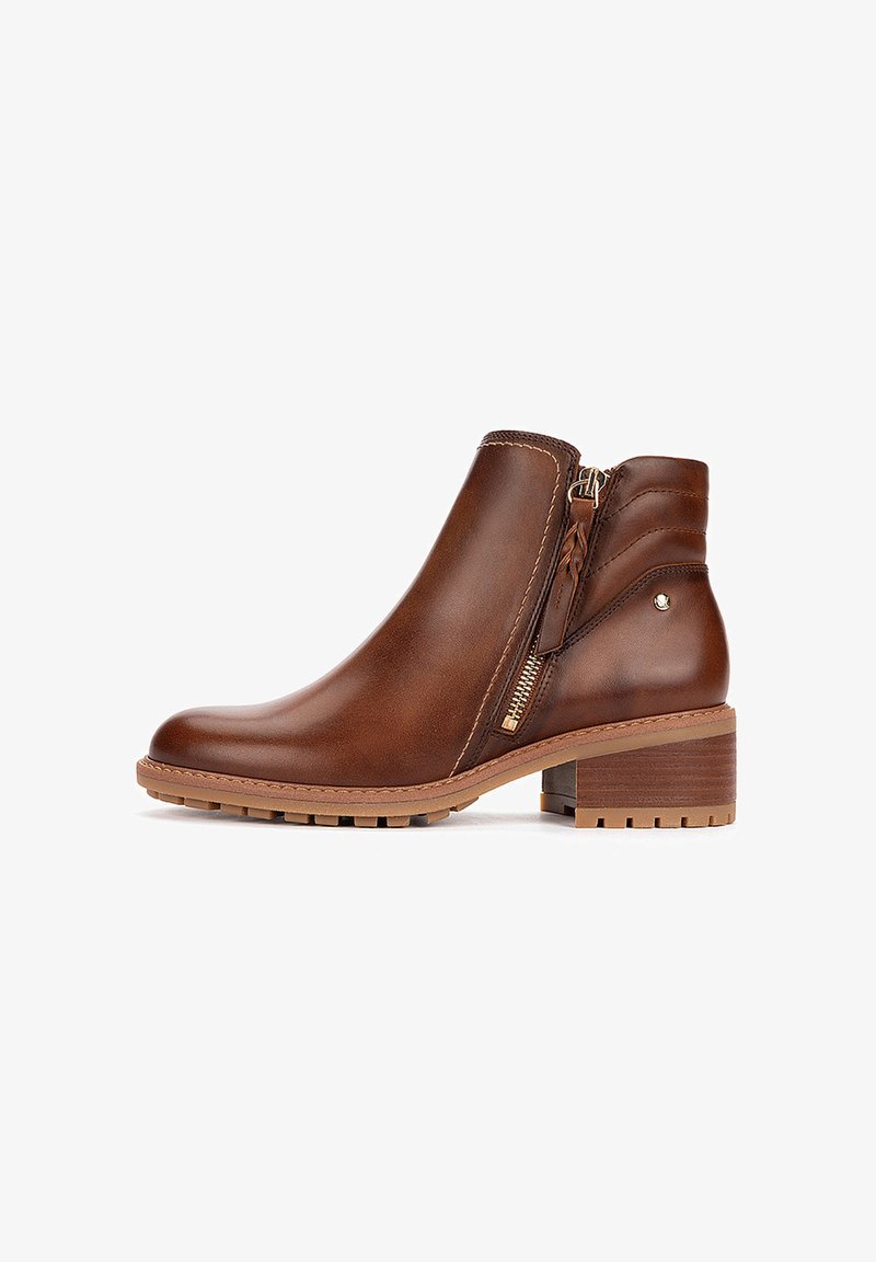 Bottine en cuir marron avec fermeture éclair latérale, talon bas empilé et semelle texturée sur fond blanc.