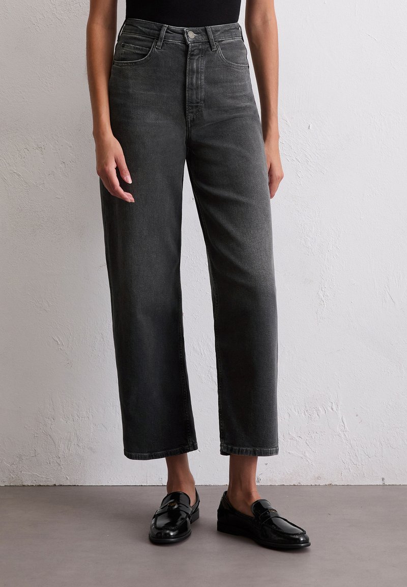 Szare dżinsy z wysokim stanem o prostym kroju nogawek, z pięcioma kieszeniami i subtelnym przetarciem. Połączone z czarnymi loafersami.