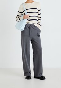 Sweter w paski w odcieniach kremowych i granatowych, szare spodnie dresowe z logo, jasnoniebieska torba na ramię, czarne buty typu chunky, casualowy strój, luźny krój.