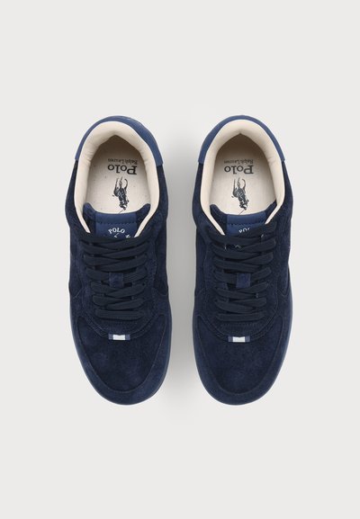 Ζευγάρι σκούρα μπλε σουέντ αθλητικά Polo Ralph Lauren με μαύρα κορδόνια και λευκή μαξιλαρωτή εσωτερική επένδυση, εμφανίζεται από πάνω.
