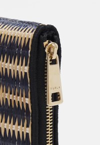Gros plan sur un coin de portefeuille tissé avec des fils noirs, beiges et bleu marine, équipé d'un curseur de fermeture éclair doré marqué Furla.