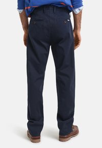 Pantalones de algodón azul marino con un corte holgado, que cuentan con bolsillos traseros con cierre de botón y una textura suave. Combinados con zapatos marrones.