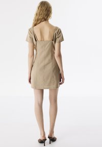 Korte beige jurk met een lage rug en korte mouwen, met een getailleerde silhouette en zichtbare naaddetails.