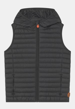 Veste matelassée noire sans manches avec capuche, fermeture éclair frontale avec tirette orange, et petite écusson rond orange près de l'ourlet du côté droit.