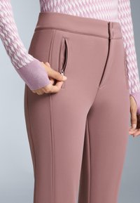 Ružičaste hlače od poliestera imaju bočni džep na patentni zatvarač, kroj prilagođen tijelu i glatku teksturu. Pojas je konturiran radi udobnosti.