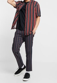 Chemise à manches courtes à boutons avec des rayures rouges et noires, associée à un pantalon rayé dans des couleurs similaires, portée avec des baskets noires.