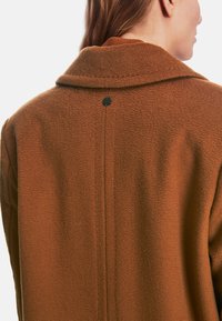 Brown wool-blend coat featuring a collar, textured fabric, and a back button detail. The design includes a central seam running down the back.