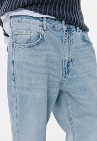 Svijetloplave traperice s opuštenim krojem, koje imaju pet džepova, pojas s petljama za remen i suptilno izblijeđivanje po cijelom materijalu.