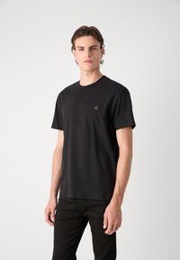 T-shirt in cotone nero con maniche corte, scollo rotondo e un piccolo logo CK ricamato sul petto. Design semplice e aderente.