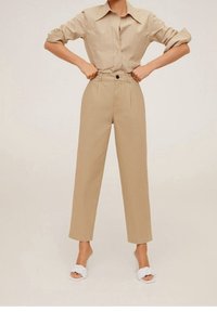 Chemise en coton beige avec col et design à boutons, associée à un pantalon beige taille haute et des sandales blanches à enfiler.